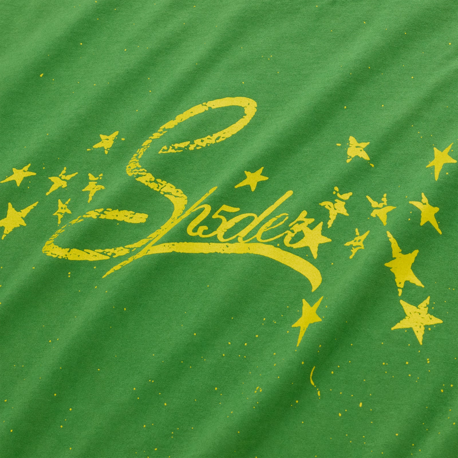 Green cotton tee with yellow "Shades" graphic and scattered stars.