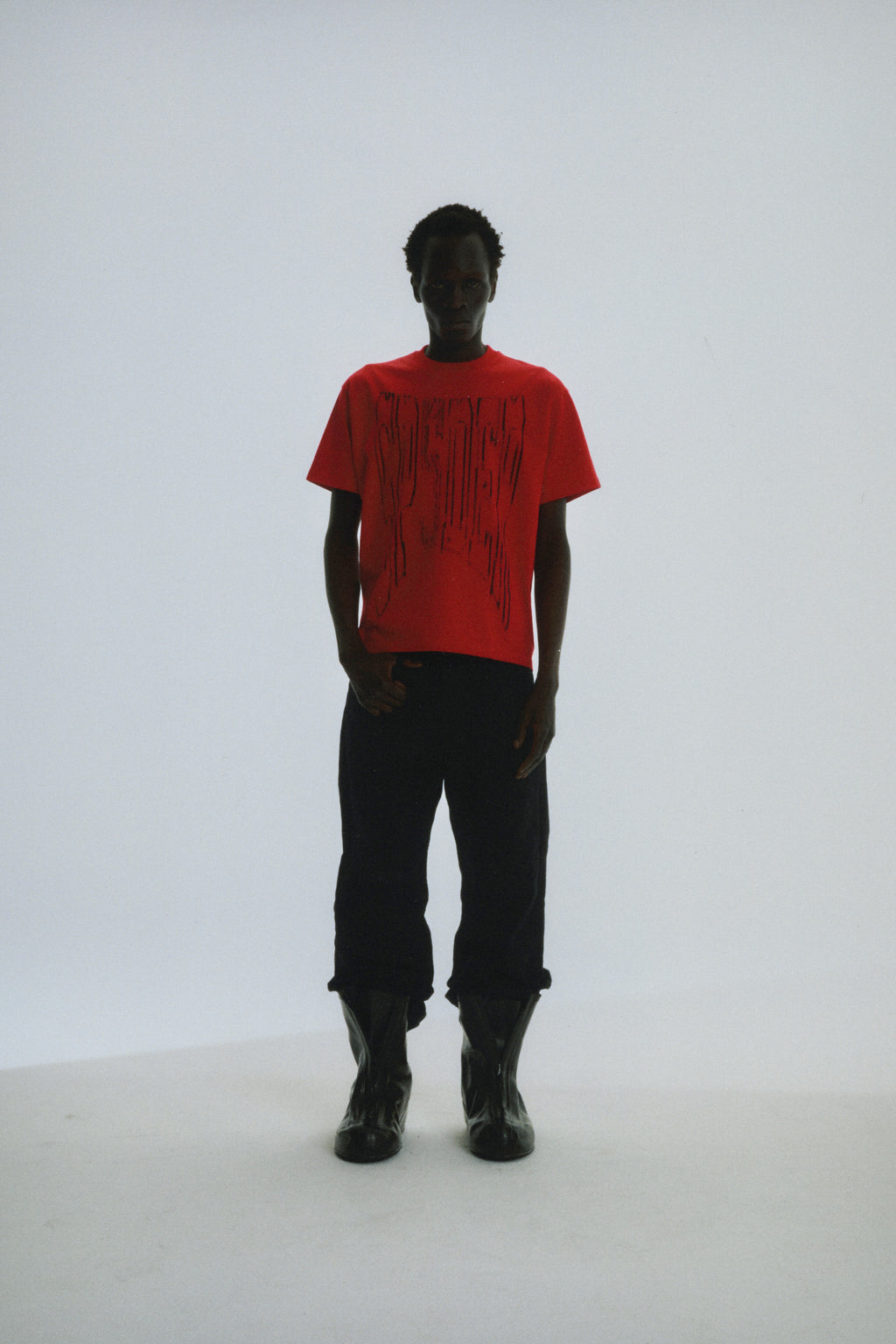 Man in red cotton tee with black graphic print, black pants, and black boots.