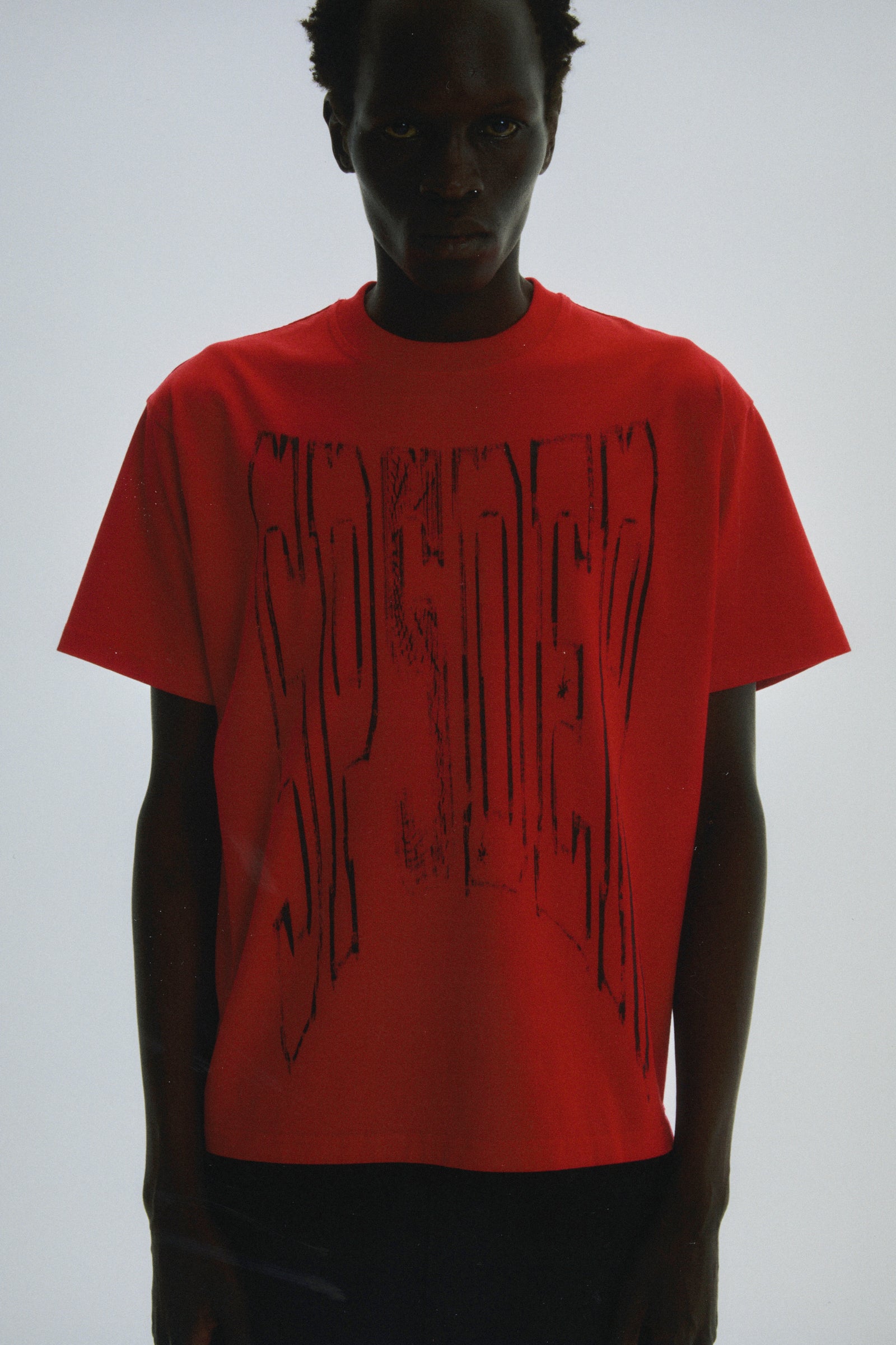 Red 100% cotton lightweight tee with a black diffused collegiate graphic print on the front.