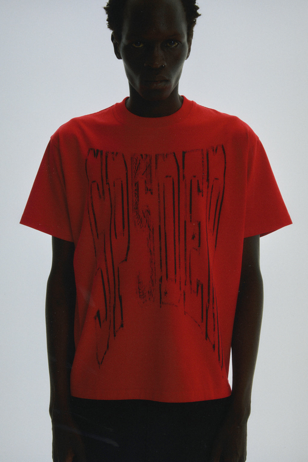 Red 100% cotton lightweight tee with a black diffused collegiate graphic print on the front.