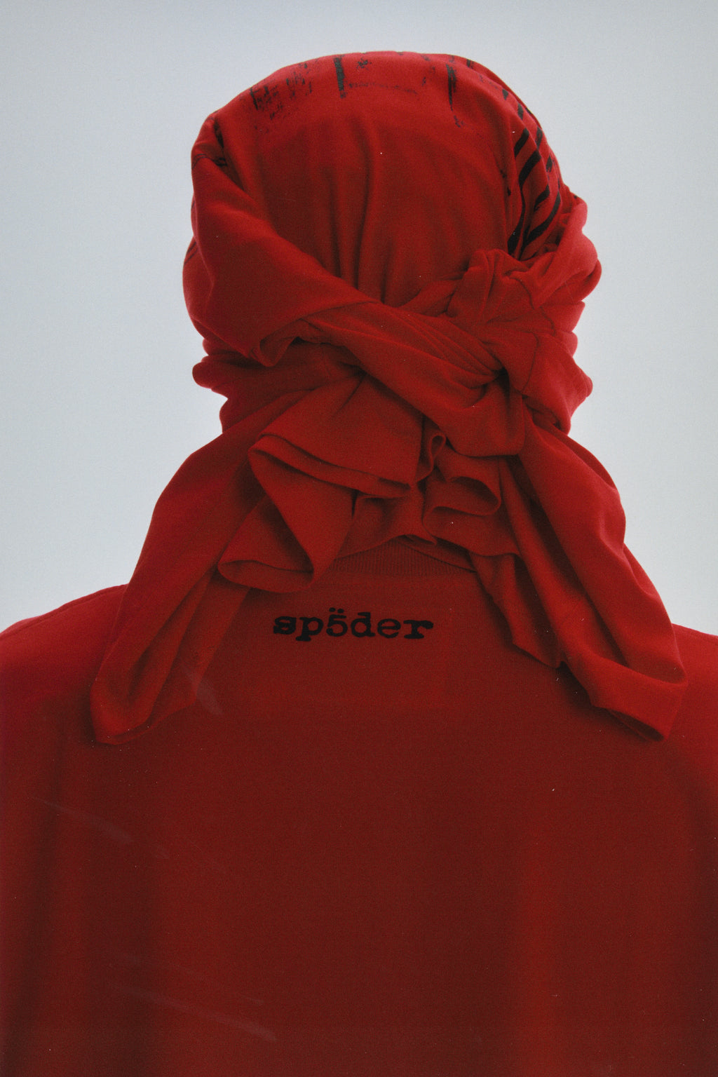Red collegiate tee with "sp5der" logo on back neck, styled with a matching red fabric headwrap.