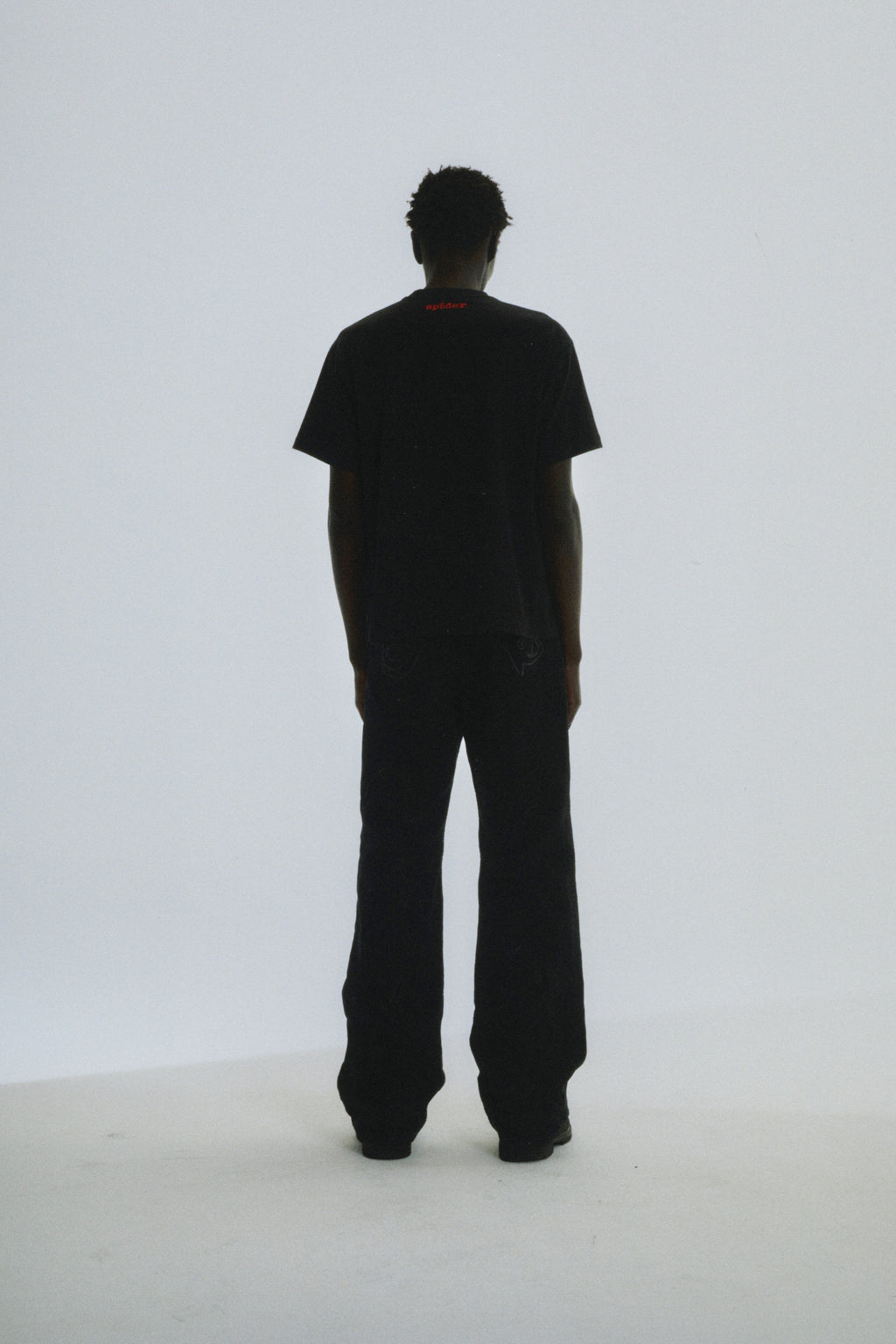 Black SP5DER Toast Tee on a model, seen from behind, with red logo on back neck.