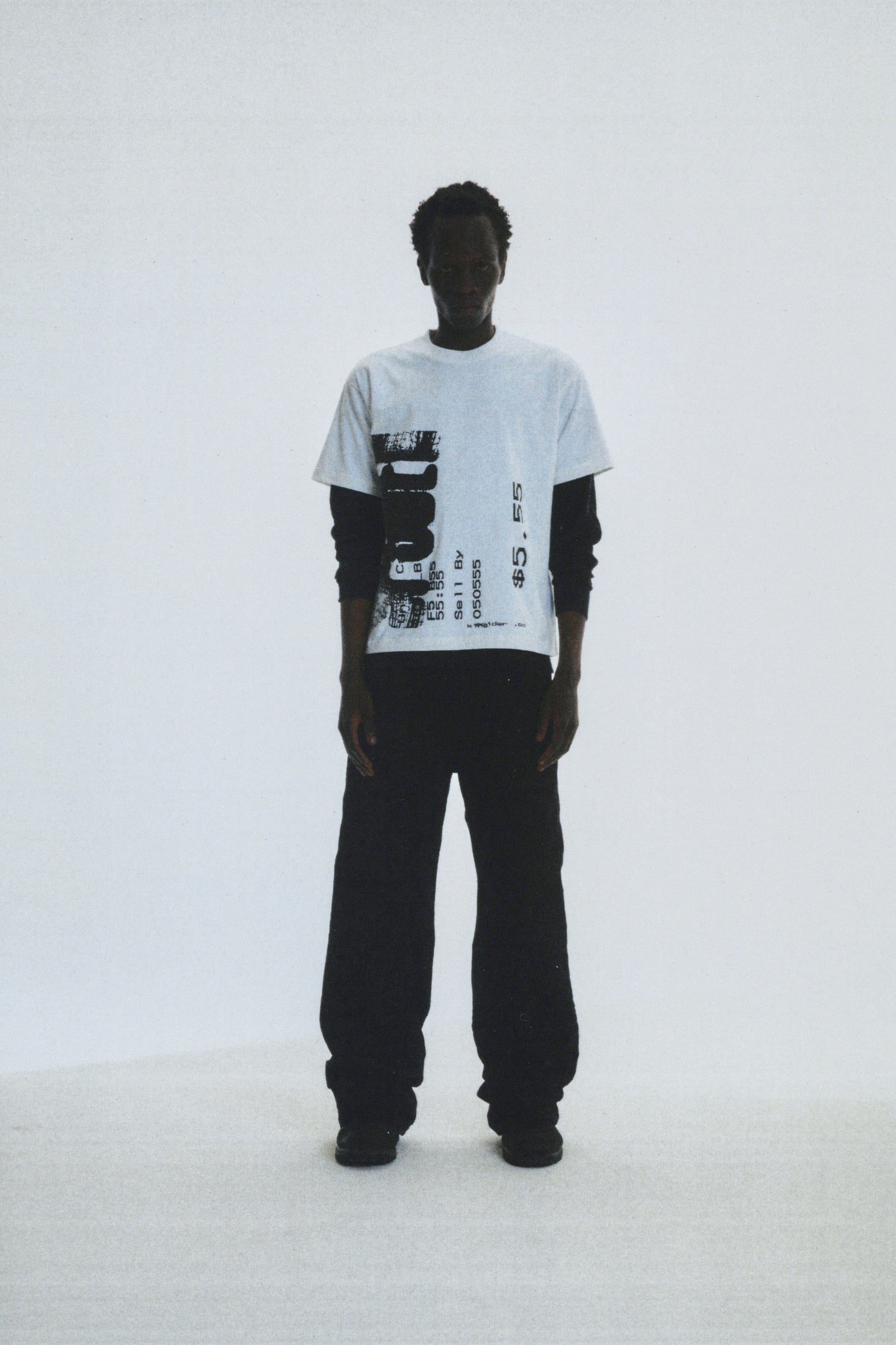 Man wearing white cotton COMMERCE TEE with black graphic print, layered over a black long-sleeve shirt.