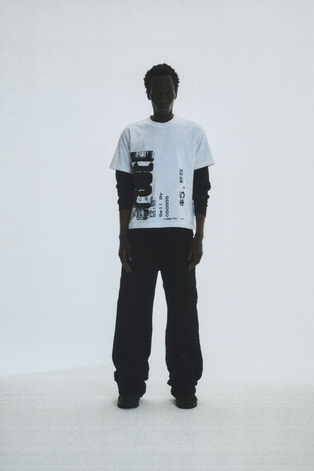 Man wearing white cotton COMMERCE TEE with black graphic print, layered over a black long-sleeve shirt.