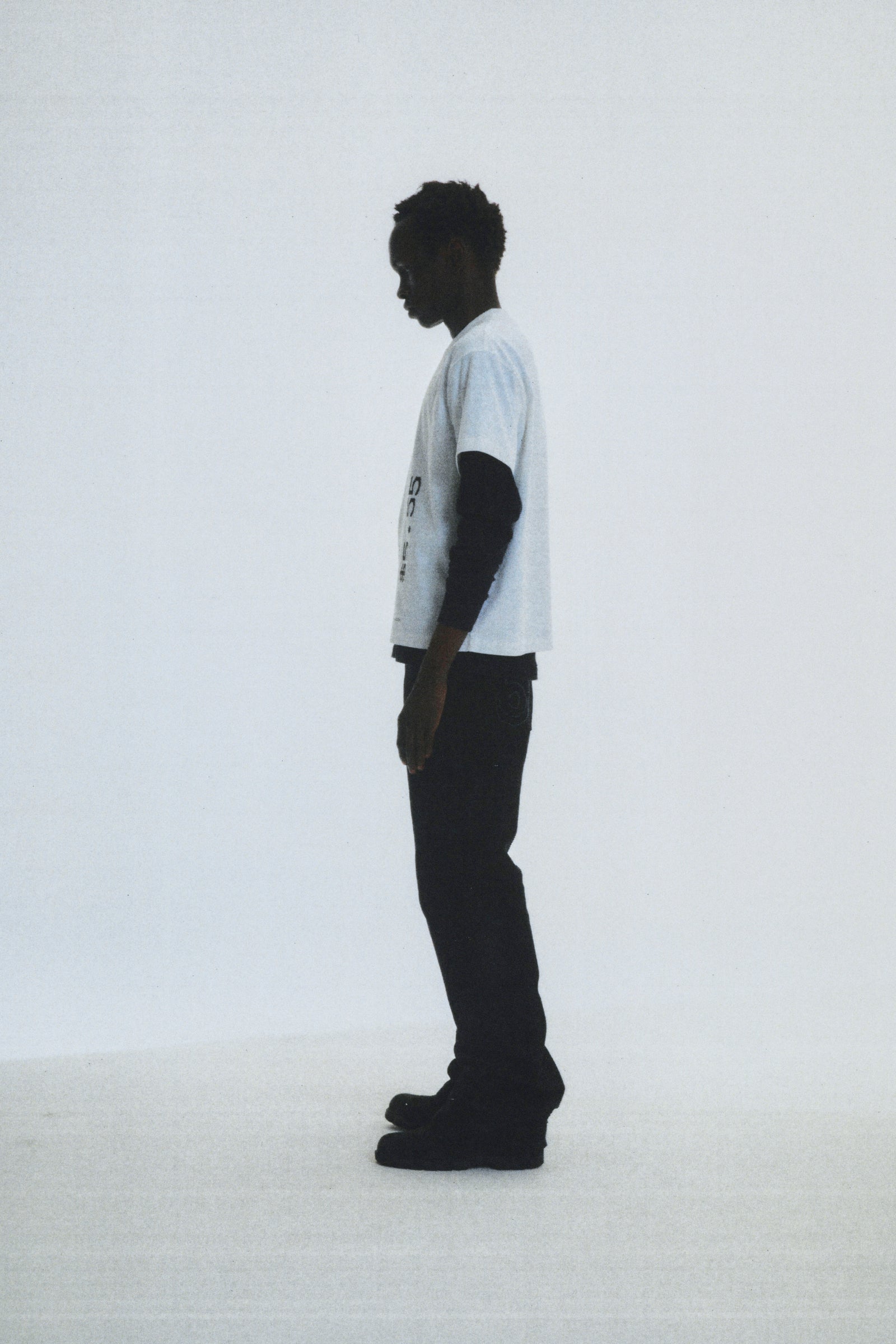 Man in a white cotton COMMERCE TEE with graphic print, black long-sleeve undershirt, and black pants.