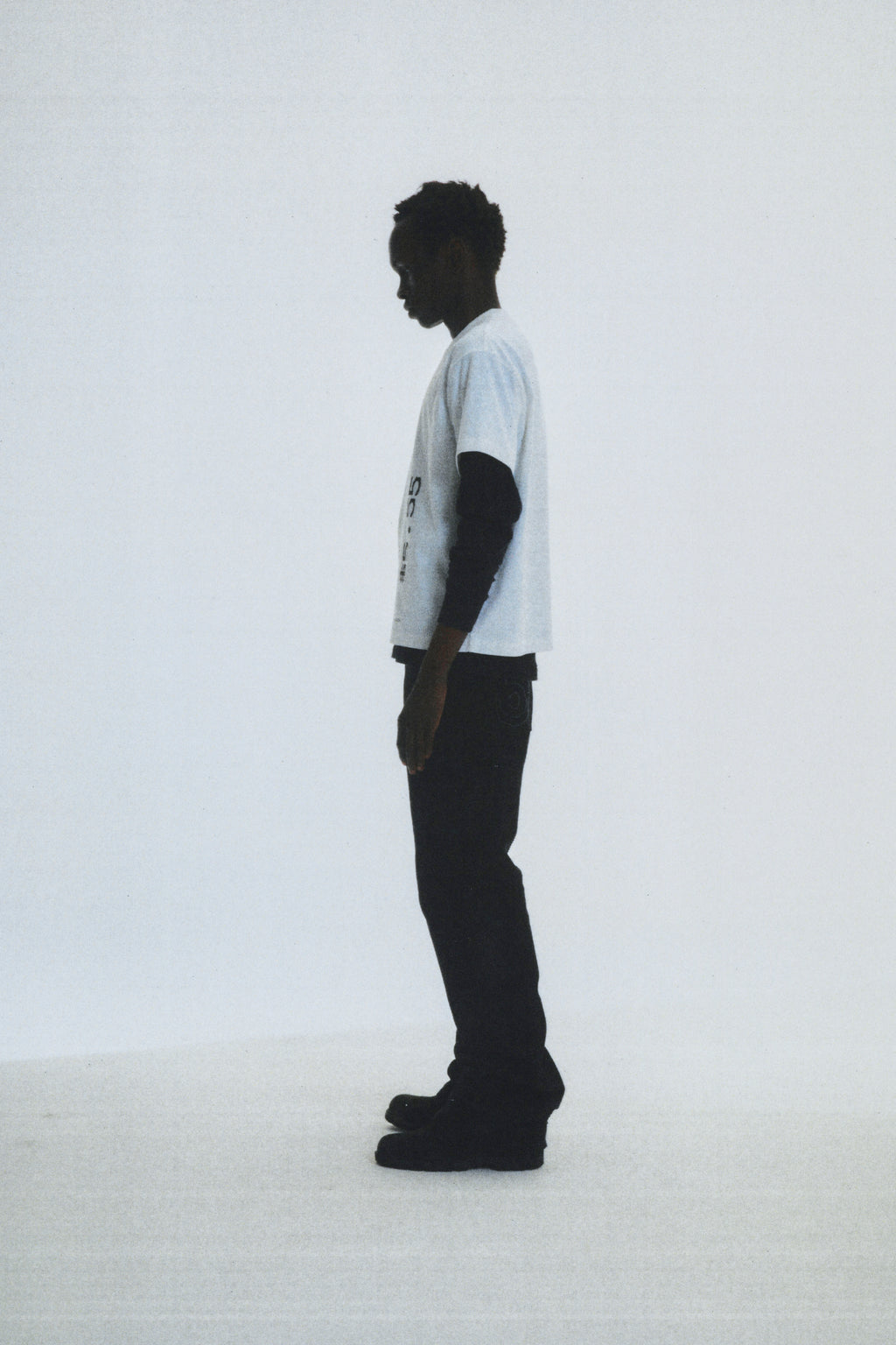 Man in a white cotton COMMERCE TEE with graphic print, black long-sleeve undershirt, and black pants.