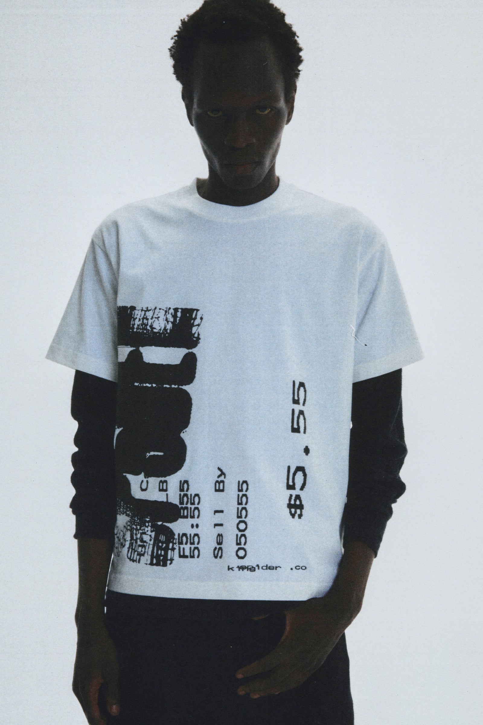 Man wearing white 100% cotton COMMERCE TEE with black graphic print, layered over a long-sleeve shirt.