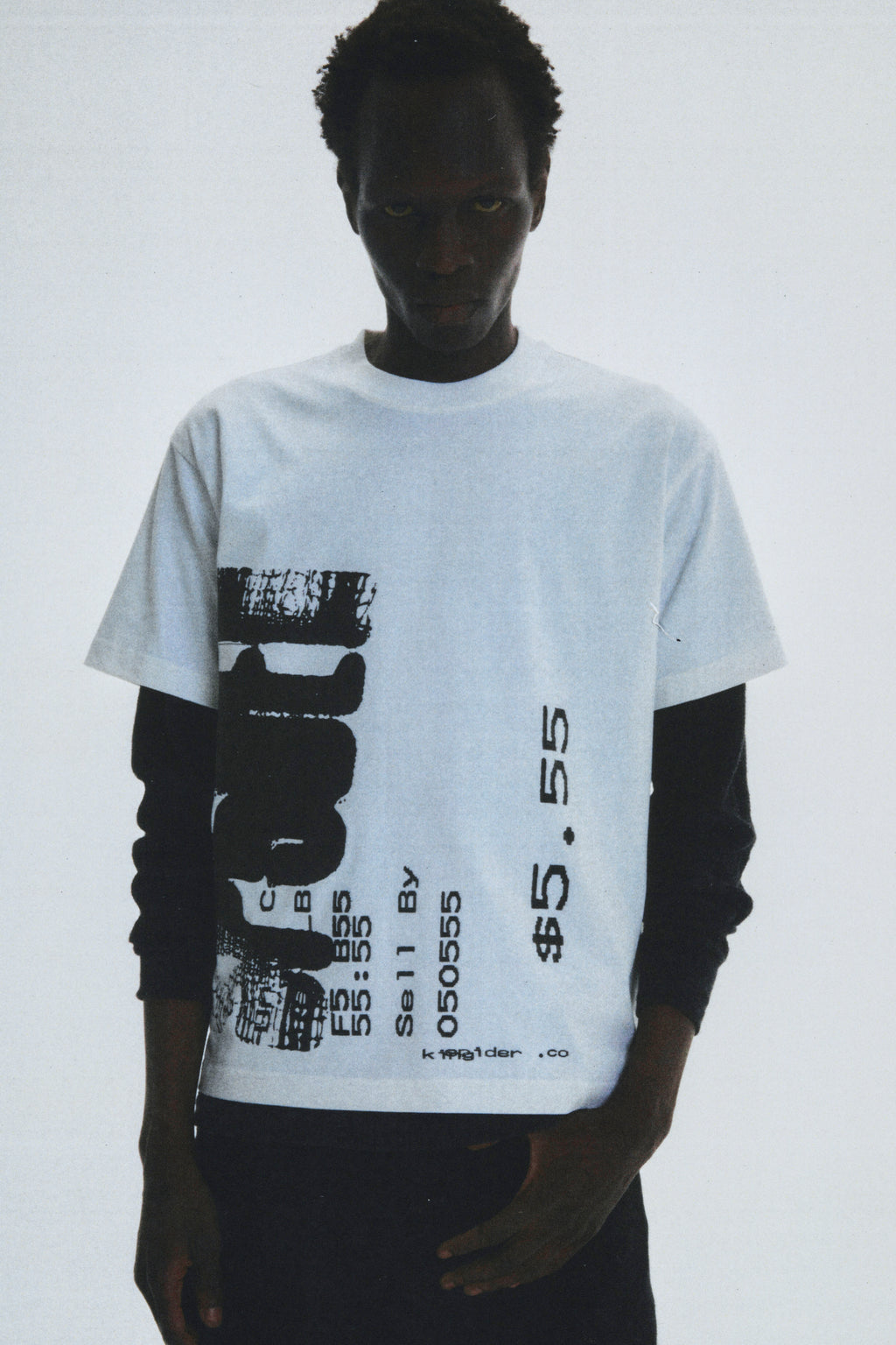 Man wearing white 100% cotton COMMERCE TEE with black graphic print, layered over a long-sleeve shirt.