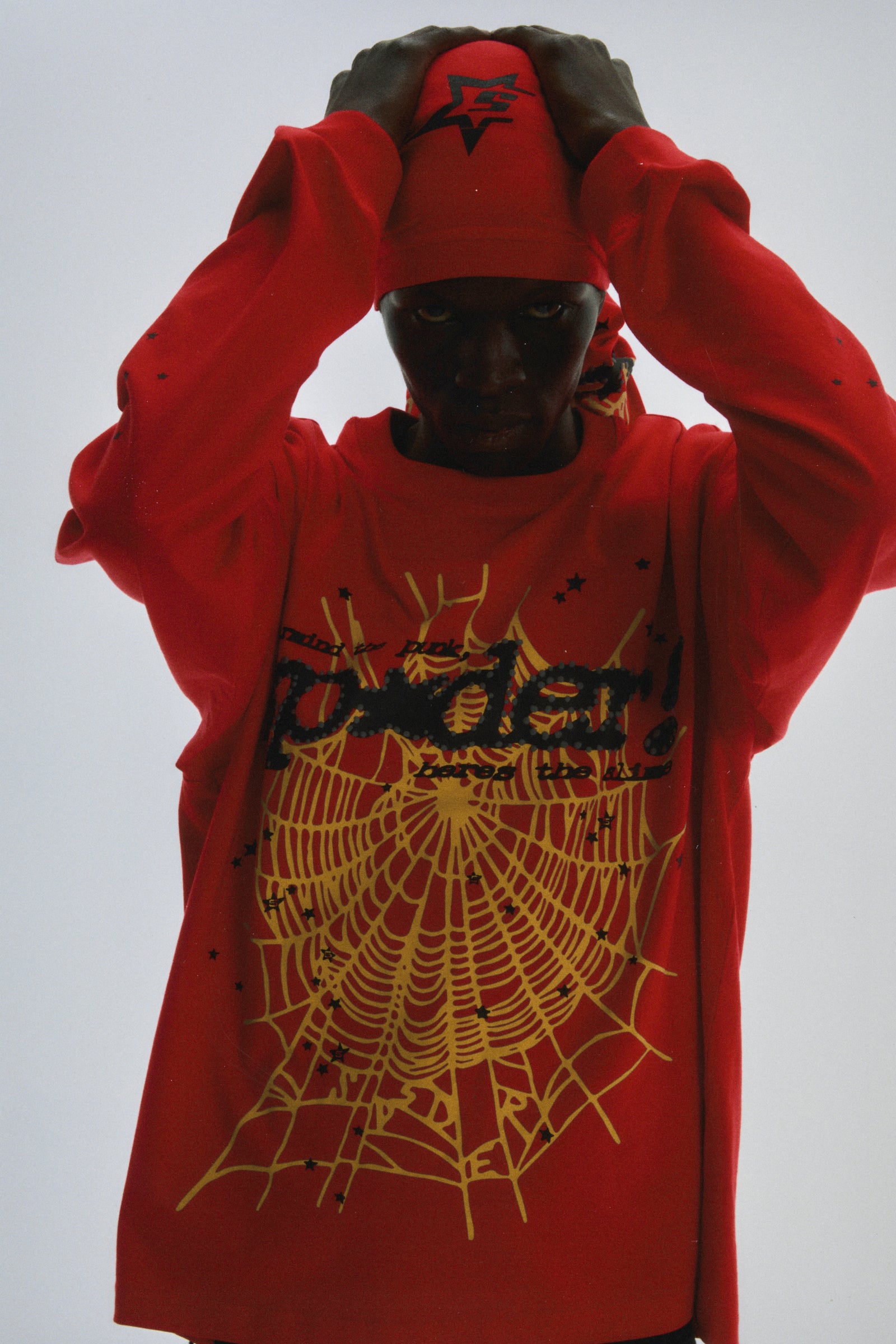 Red PUNK V2 LONGSLEEVE with yellow spiderweb & SP5DER motif, scattered stars, worn by a person.