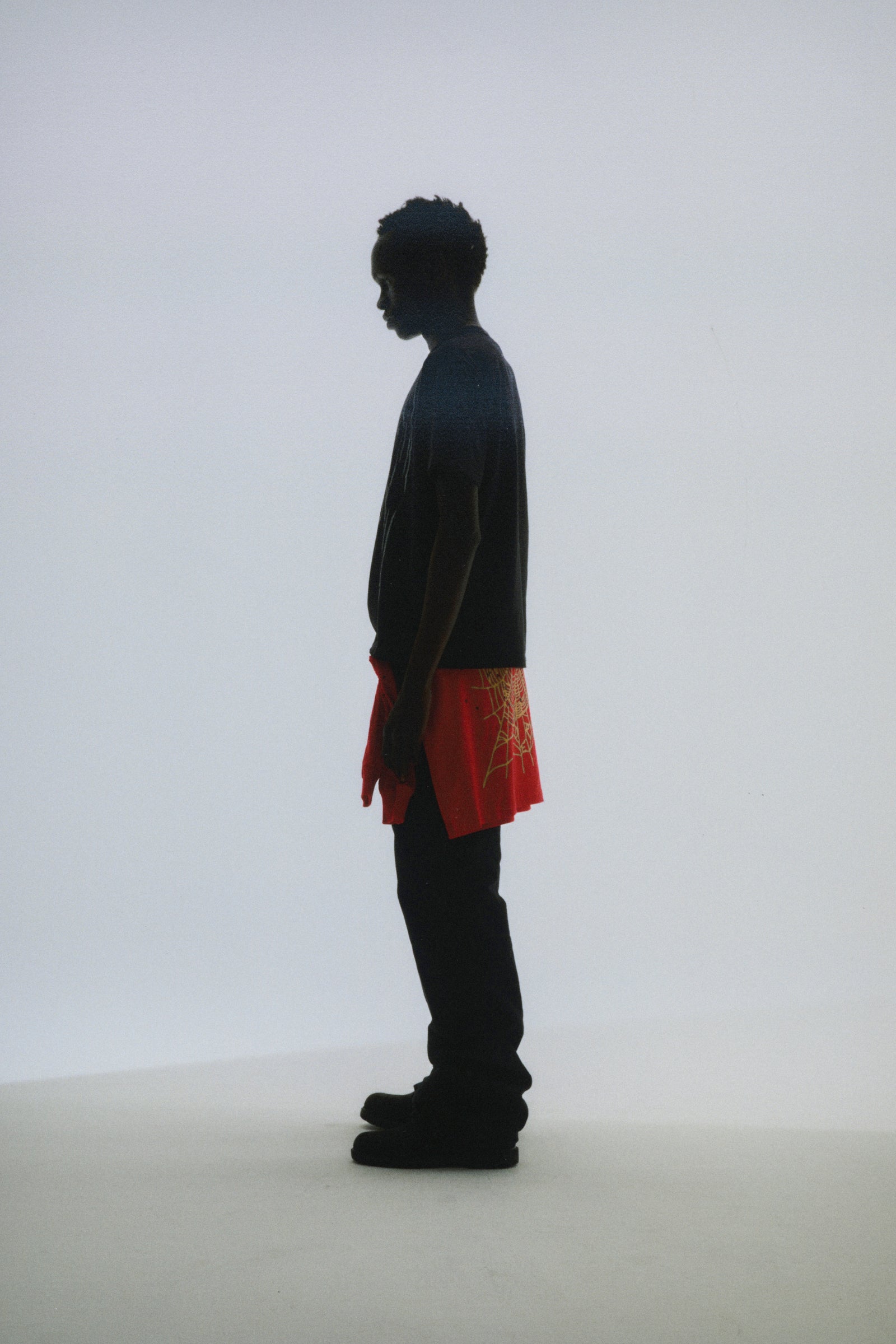 Silhouette of a person wearing a dark tee and bright orange shorts with a spiderweb graphic.