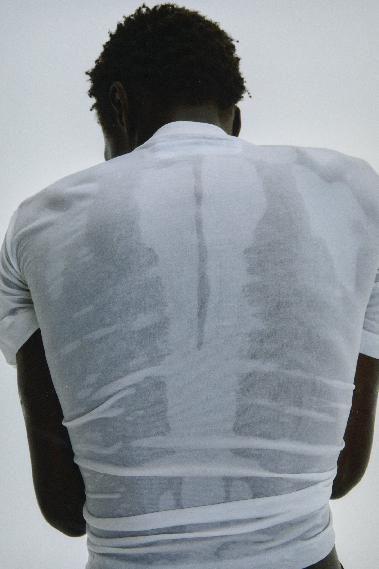 Back view of a man wearing a wet, white 100% cotton lightweight tee, showing the fabric clinging to his back.