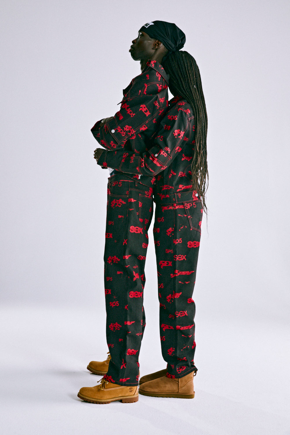 Two people in black denim jackets and pants with red "SEX" all-over print, red contrast stitching.
