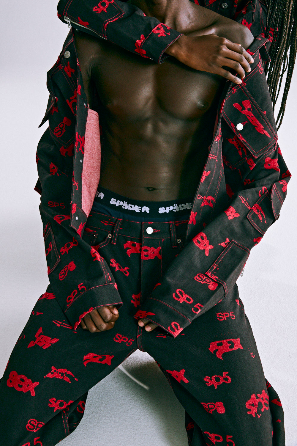 Black denim pants and jacket with red all-over SP5DER print, red contrast stitching, and branded hardware.