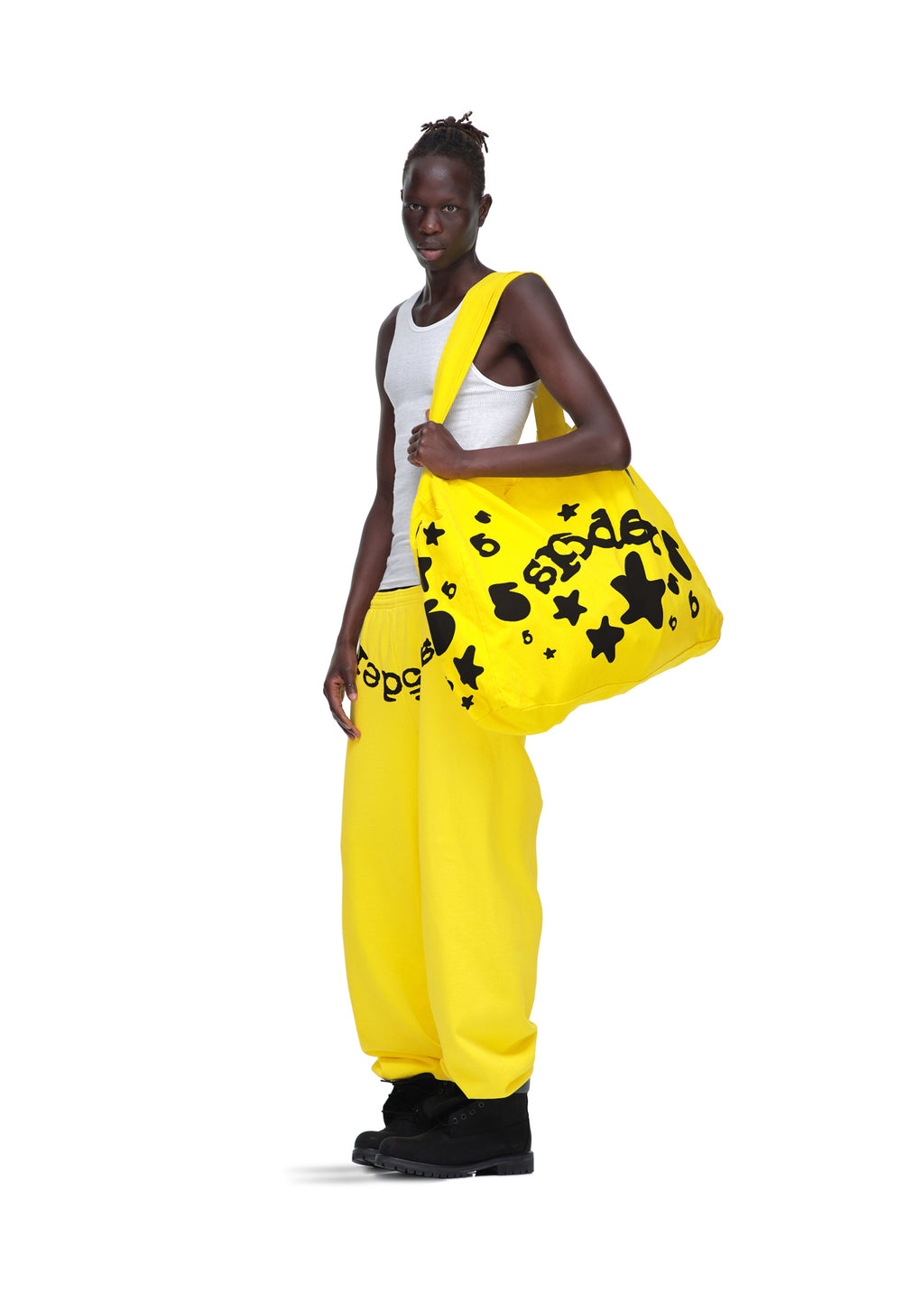 Model in a white tank top and yellow sweatpants holding a bright yellow Beluga twill tote bag with black star and text print.