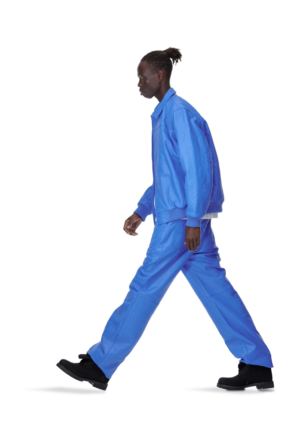 Male model in blue debossed web leather pant and matching jacket, black shoes, walking left.