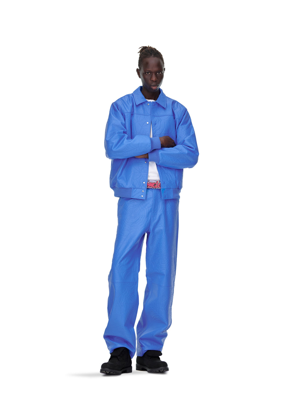 Male model in blue debossed web leather pant and matching jacket, white shirt, black shoes.