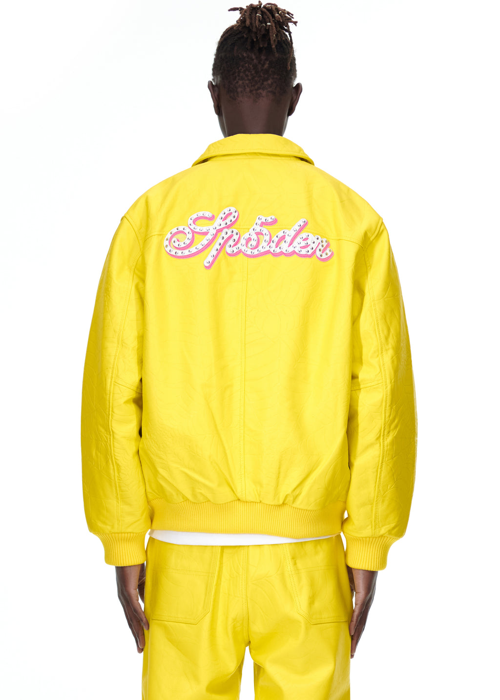 Back view of a male model wearing a yellow debossed web cowskin leather jacket with pink studded text.