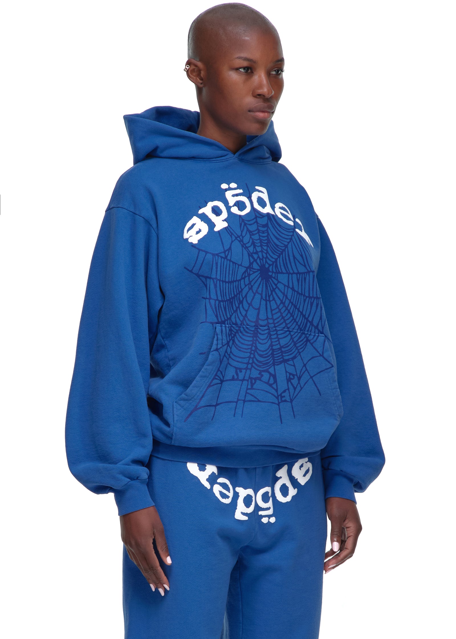 Female model in a blue Legacy Hoodie with white OG SP5DER V2 text and web puff/discharge print.