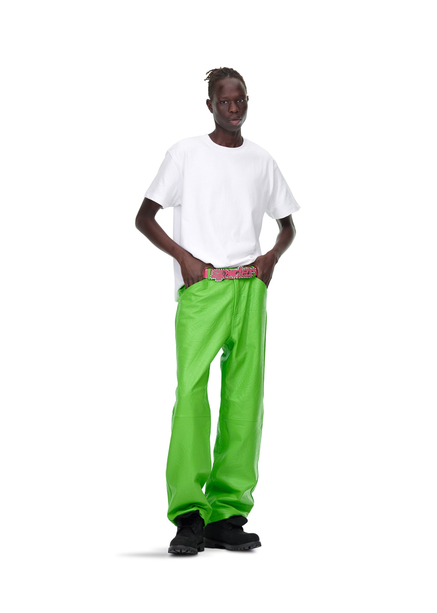 Male model in bright green debossed web leather pants with a pink suede logo patch, white t-shirt, and black boots.