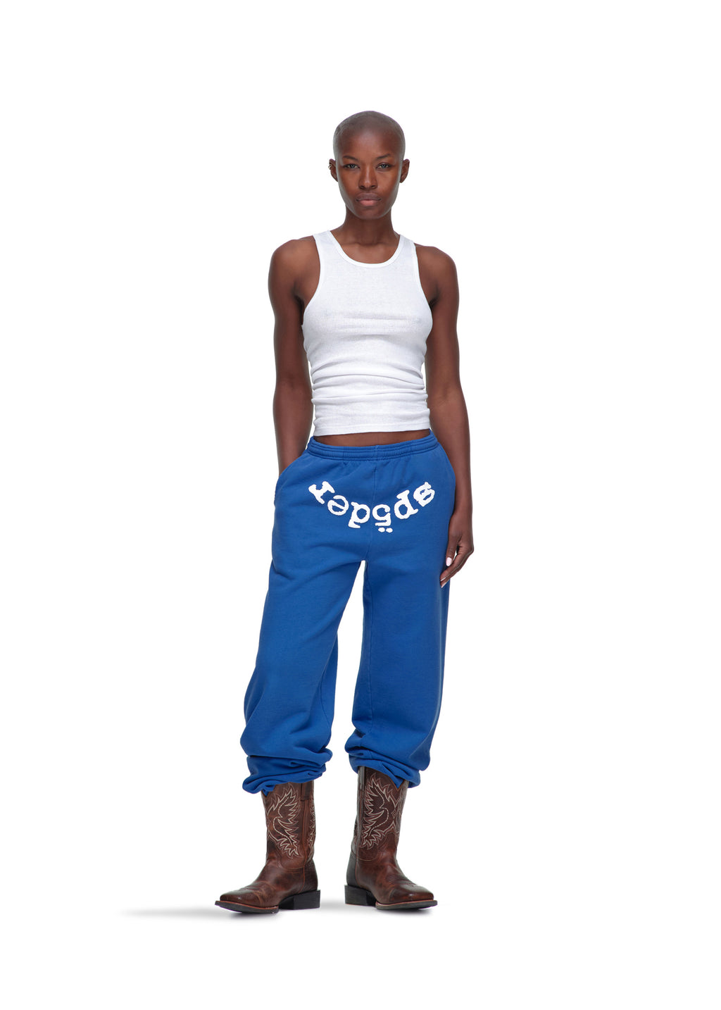 Female model in blue 23oz fleece LEGACY SWEATPANT with white "sp5der" puff print, white ribbed tank, and cowboy boots.