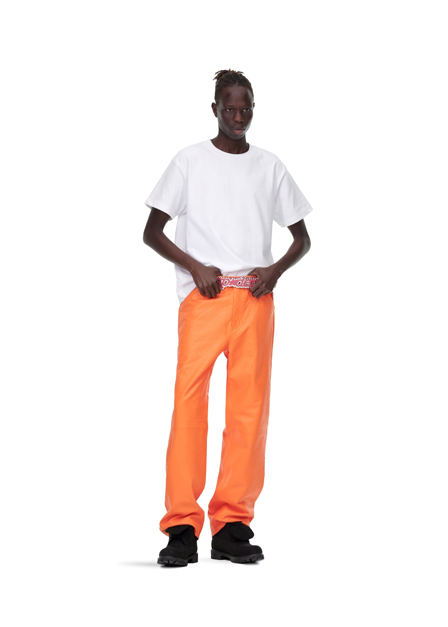 Male model in orange debossed web leather pants, white tee, and black shoes.