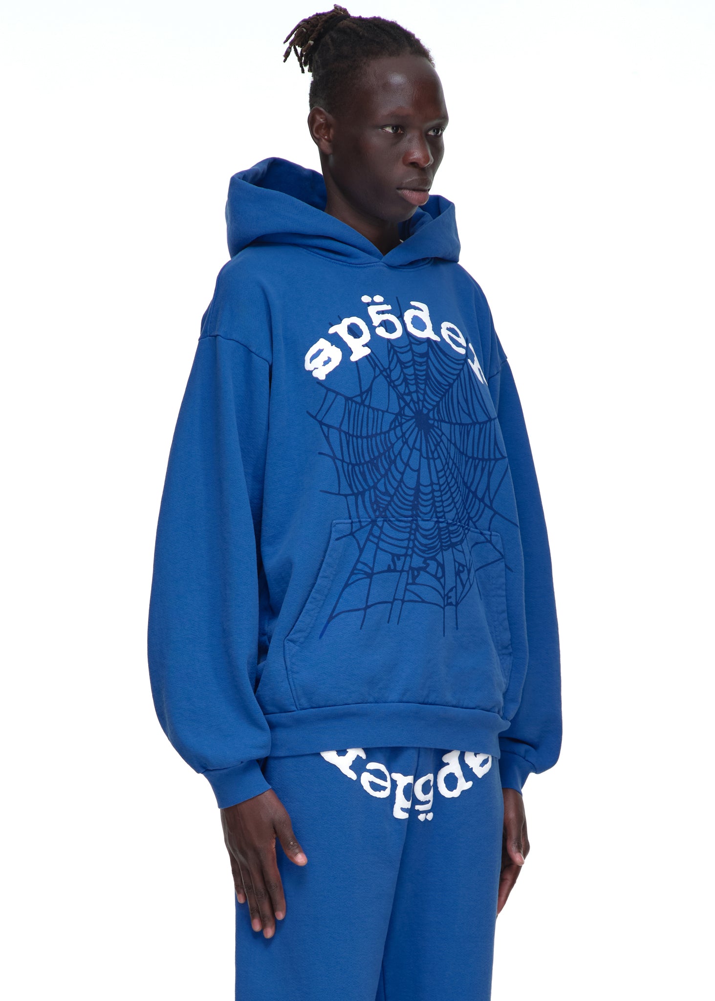 Male model in blue LEGACY HOODIE with white SP5DER text and web print, matching sweatpants.