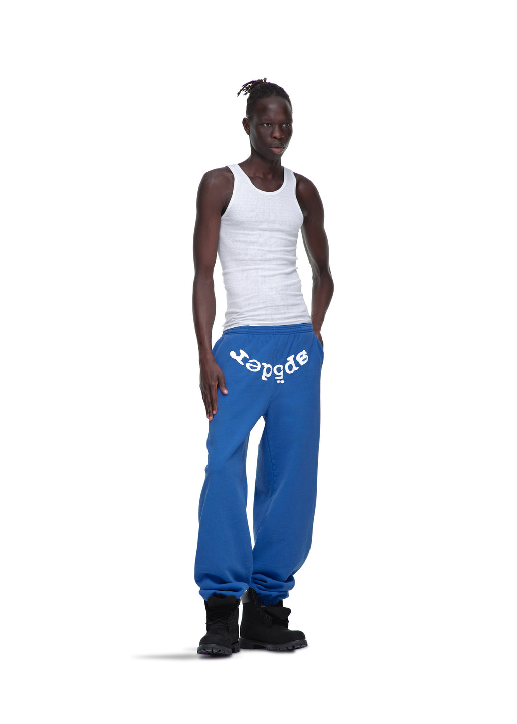Male model in blue LEGACY SWEATPANT with white "sp5der" puff print, white tank top, and black boots.