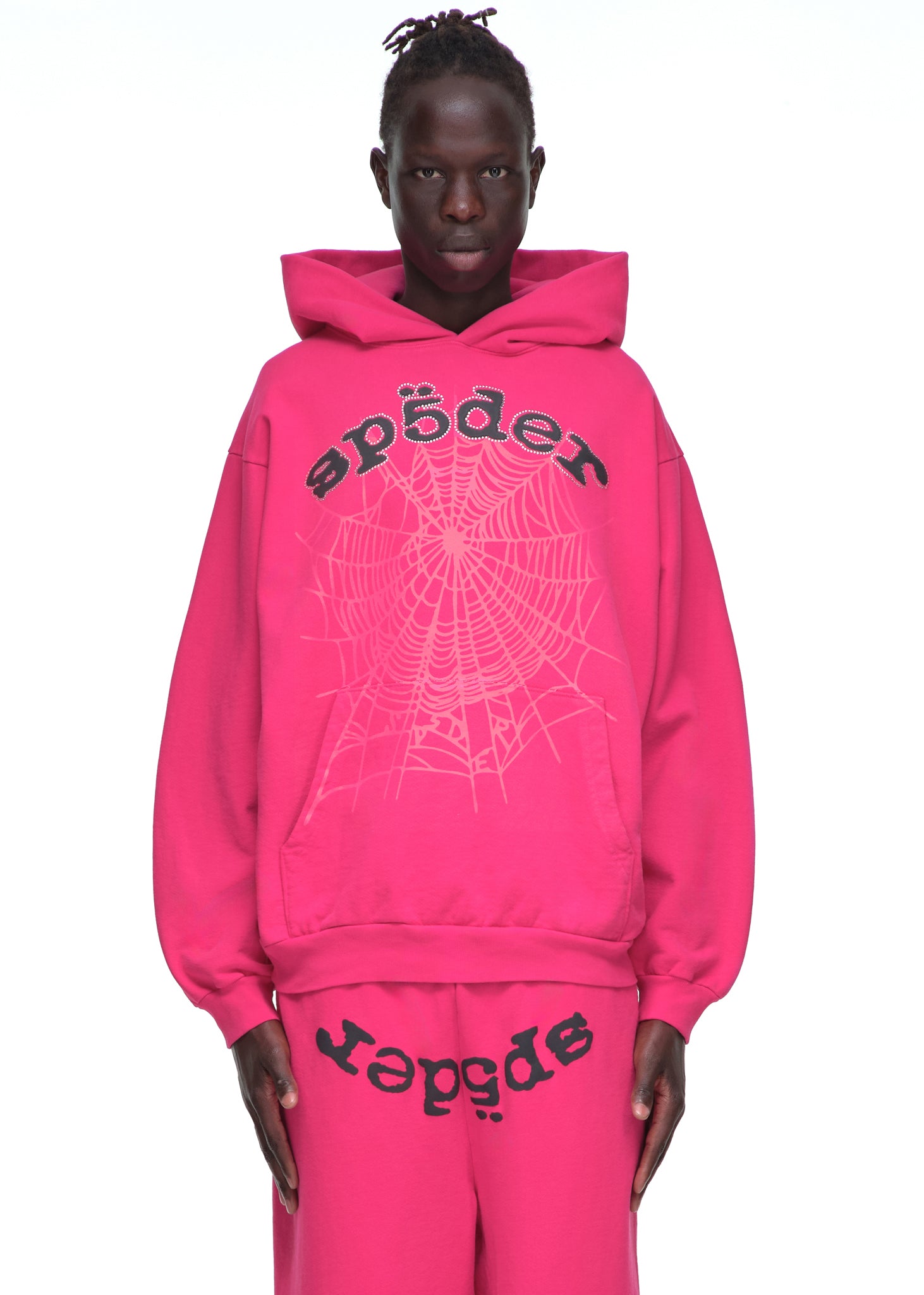 Male model in a bright pink LEGACY HOODIE with rhinestone SP5DER text and web print.
