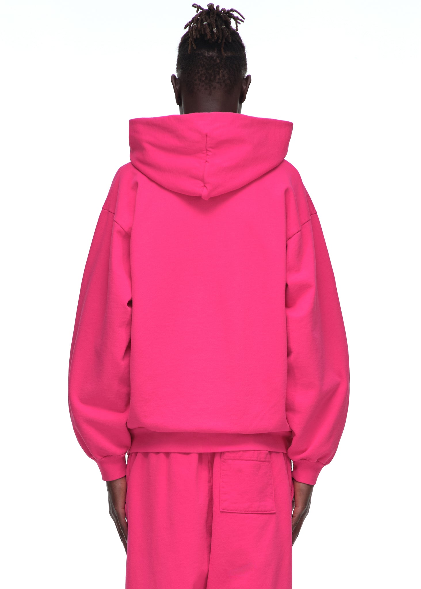 Back view of a male model wearing a bright pink LEGACY HOODIE and matching sweatpants.