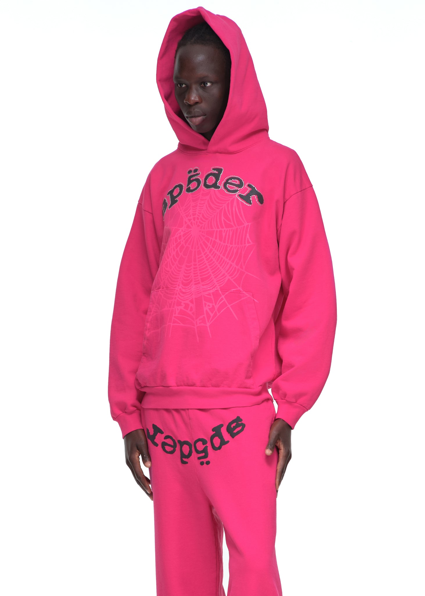 Male model in a pink Legacy Hoodie with black rhinestone "SP5DER" text and web print.