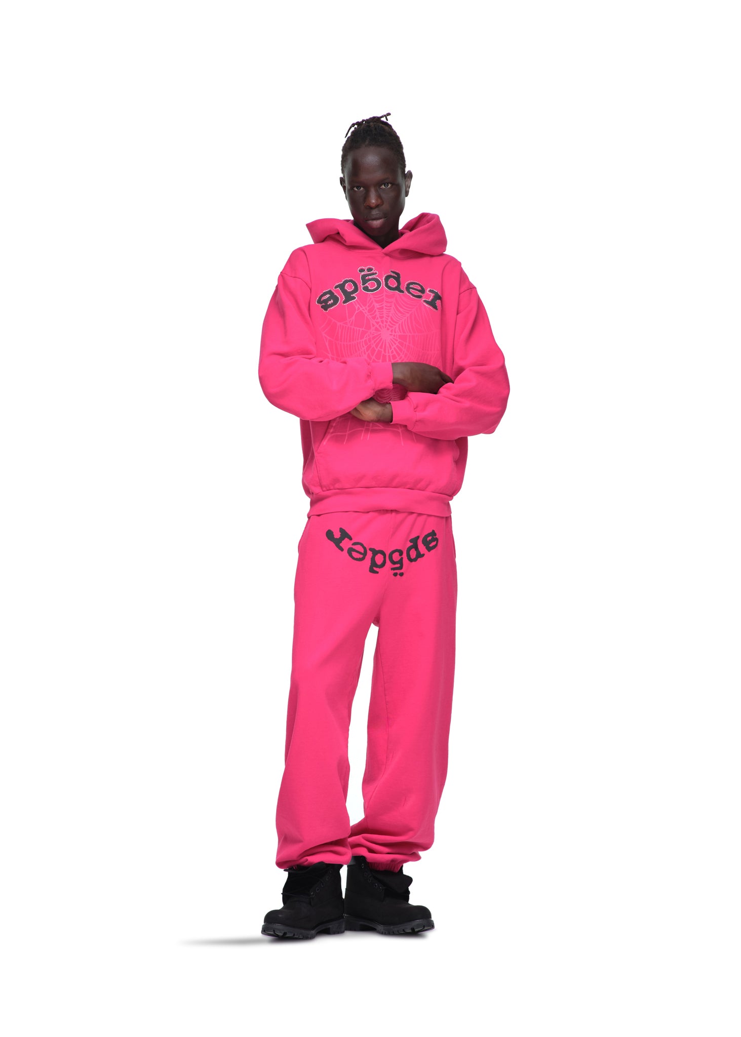 Male model in a hot pink LEGACY HOODIE and sweatpants with black SP5DER text and web print.