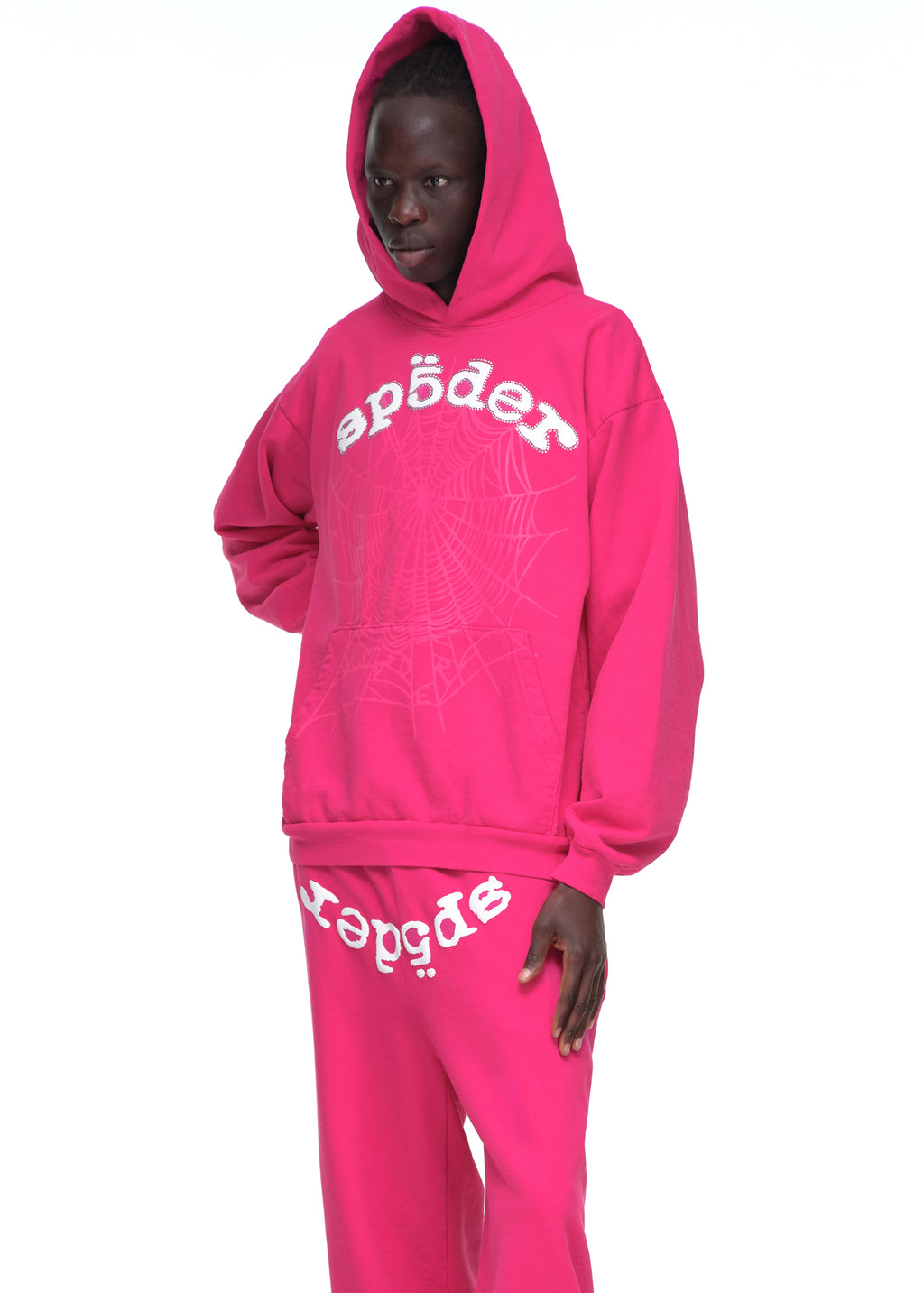 Male model in pink Legacy Hoodie and sweatpants with rhinestone SP5DER logo and web print.