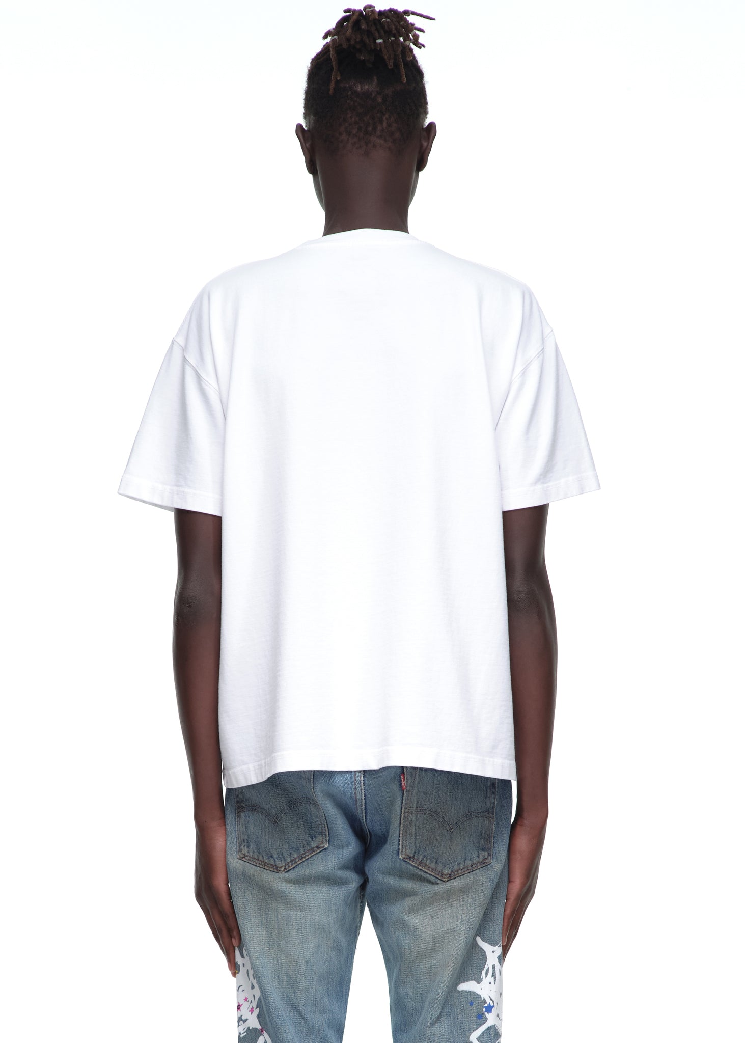 Male model in standard fit white 14oz cotton Souvenir Tee and distressed jeans, back view.