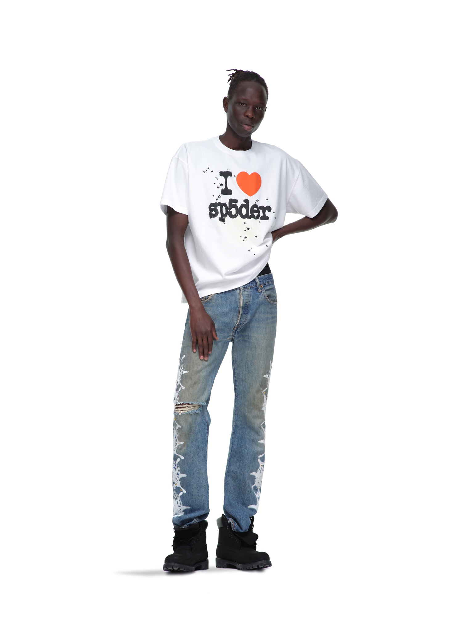 Male model in white 14oz cotton SOUVENIR TEE with "I ❤️ sp5der" graphic, distressed jeans, and black boots.