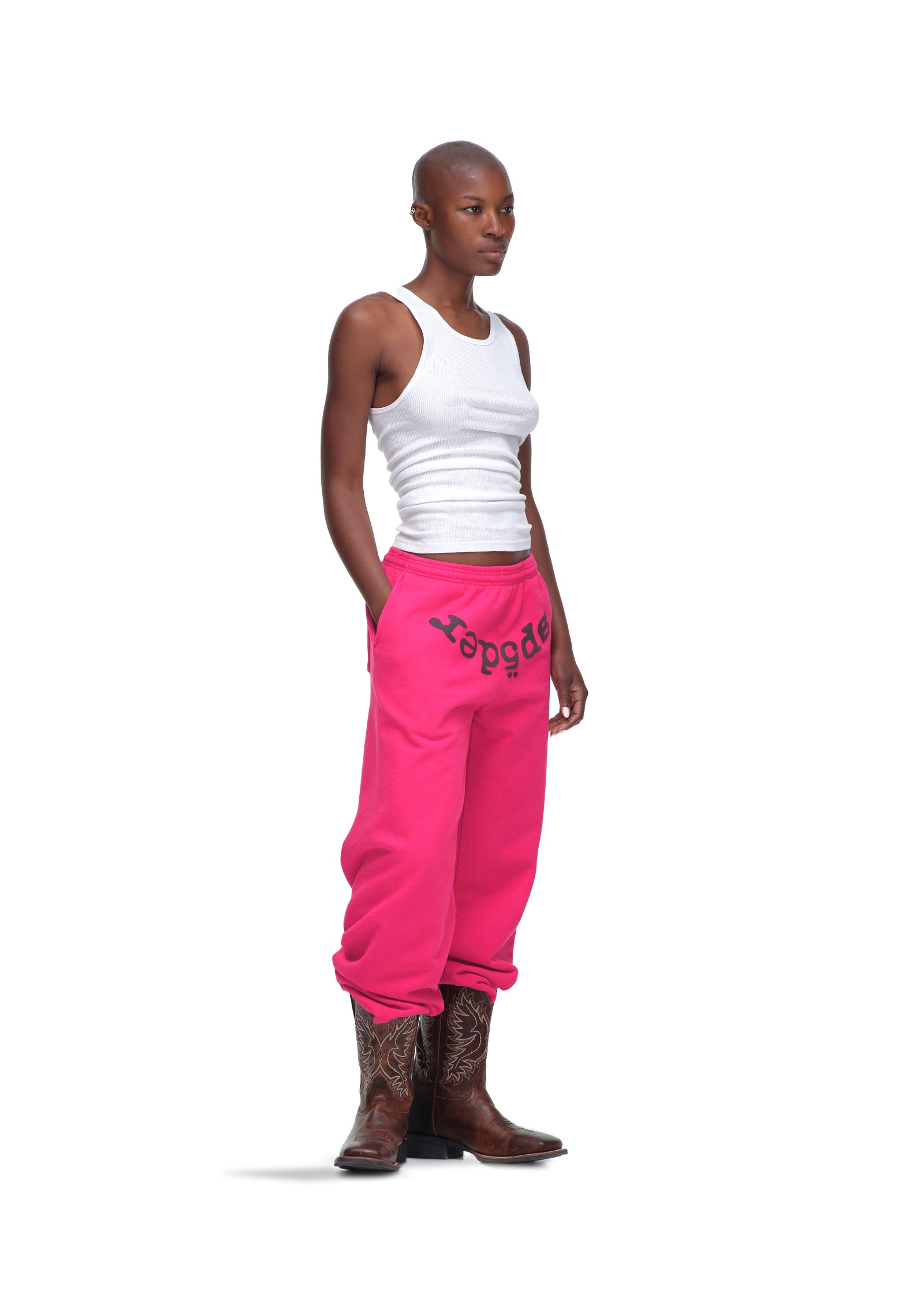 Female model in hot pink LEGACY SWEATPANT with "sp5der" puff print, white tank top, and cowboy boots.