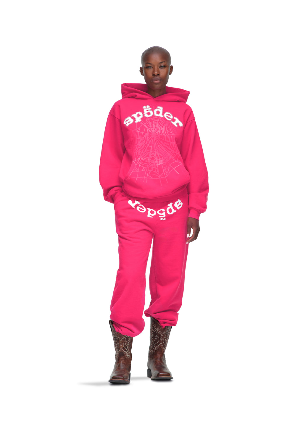 Female model in a pink Legacy Hoodie and sweatpants with white spider web and text print, wearing cowboy boots.