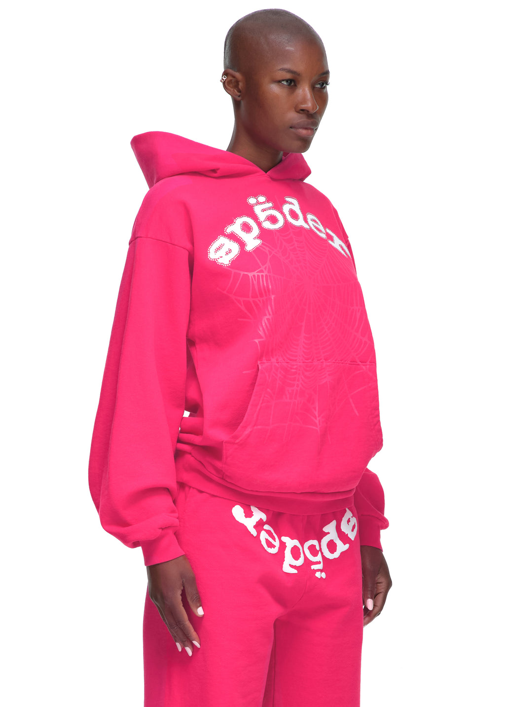 Female model in a bright pink Legacy Hoodie and sweatpants with rhinestone SP5DER logo and web print.