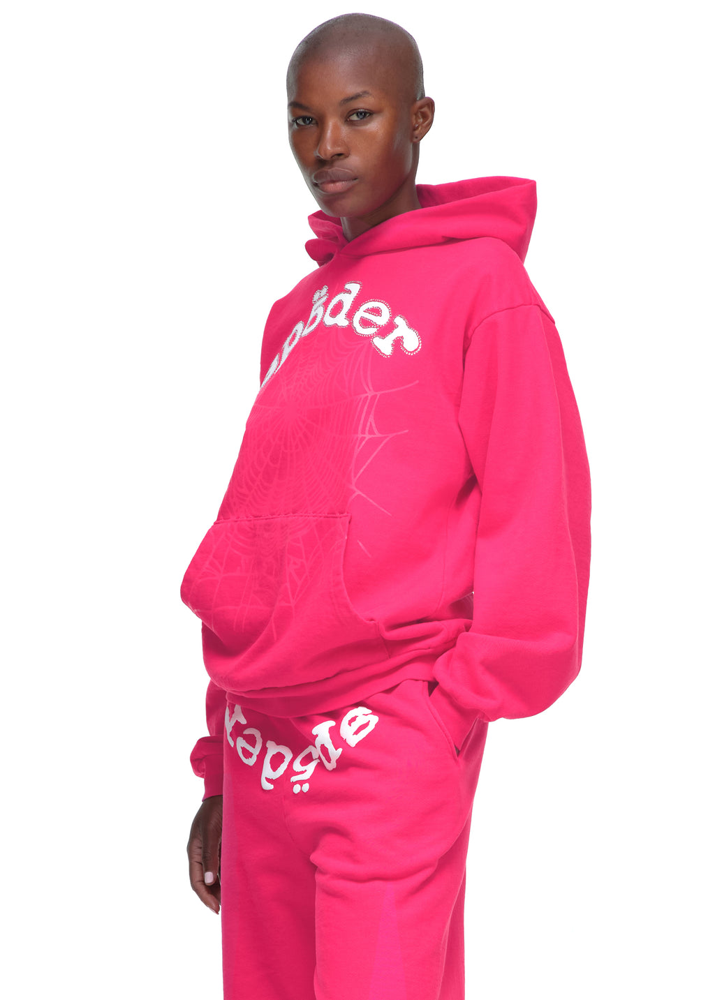 Male model in a pink LEGACY HOODIE with white puff print "Sp5der" text, discharge web, and matching sweatpants.