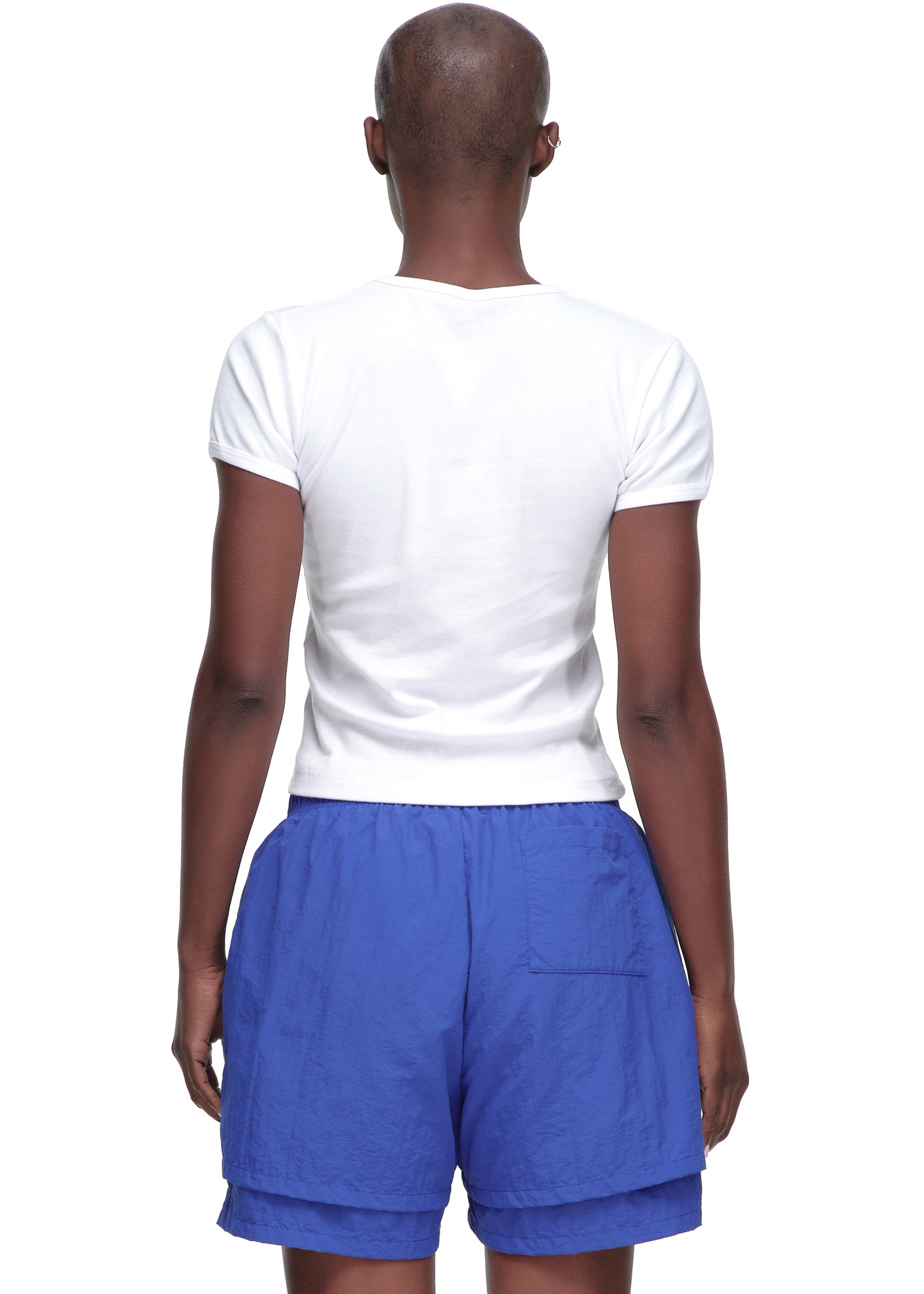 Back view of a female model wearing a plain white, cropped fitted 100% cotton baby tee.