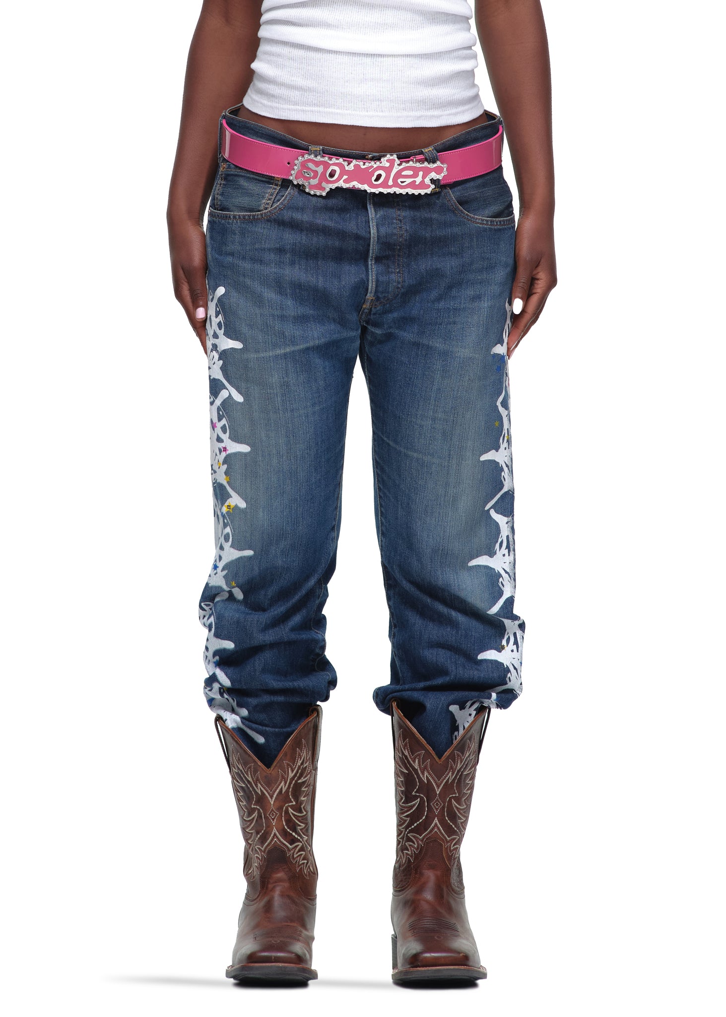 P*NK V2 BELT: Pink patent leather belt with rhinestone "SP5DER" buckle, worn with jeans and cowboy boots.