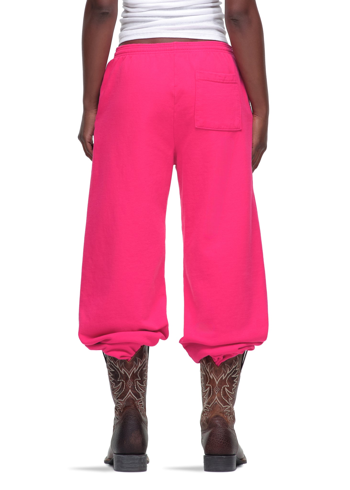 Rear view of a person wearing bright pink LEGACY SWEATPANTS made from 23oz fleece, with a back pocket, paired with cowboy boots.