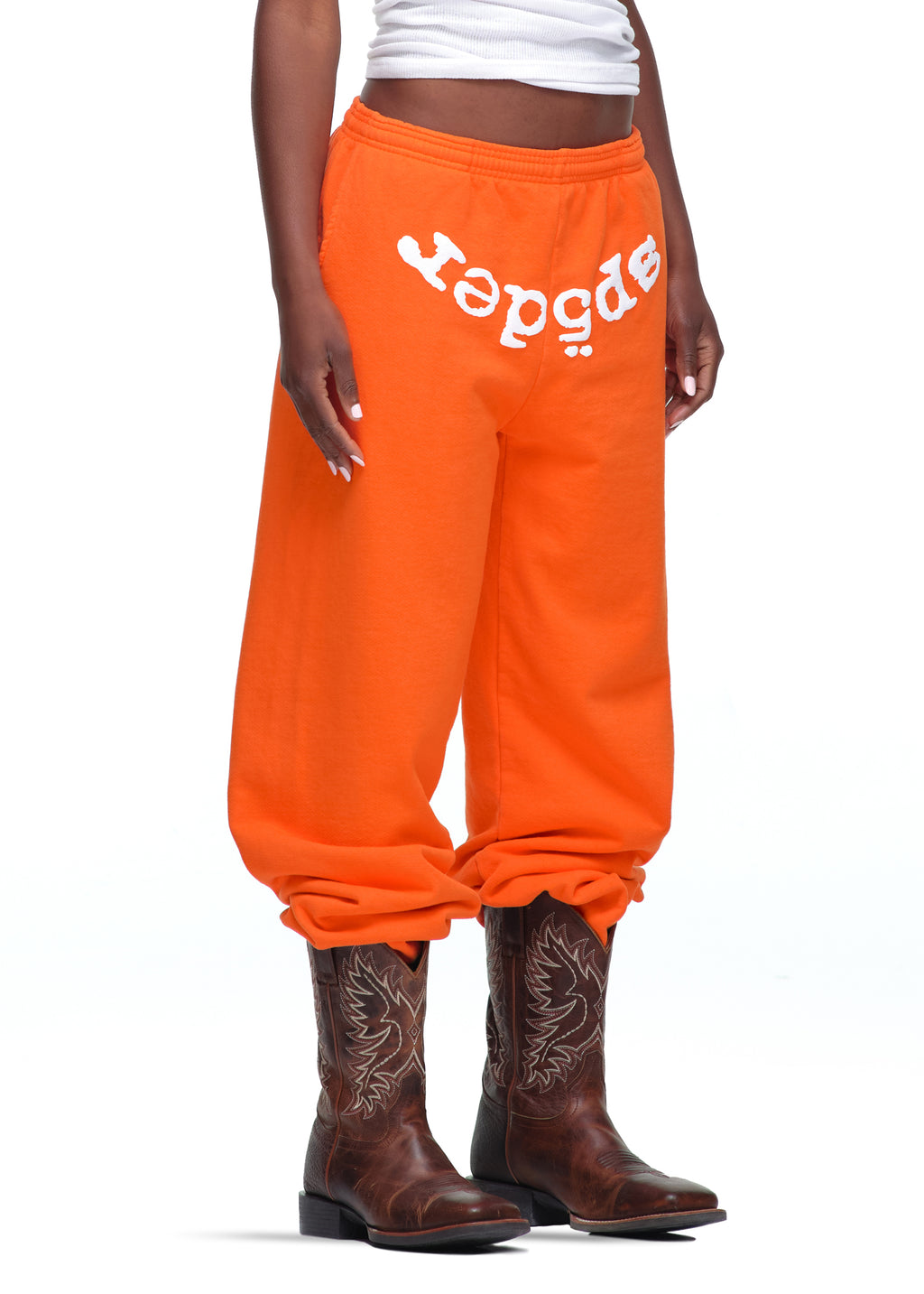 Orange 23oz fleece Legacy Sweatpants with white "sp5der" puff print, worn with cowboy boots.