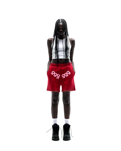 Model in red 13oz cotton fleece Angel Number shorts with white print, drawcord, and raw hem.