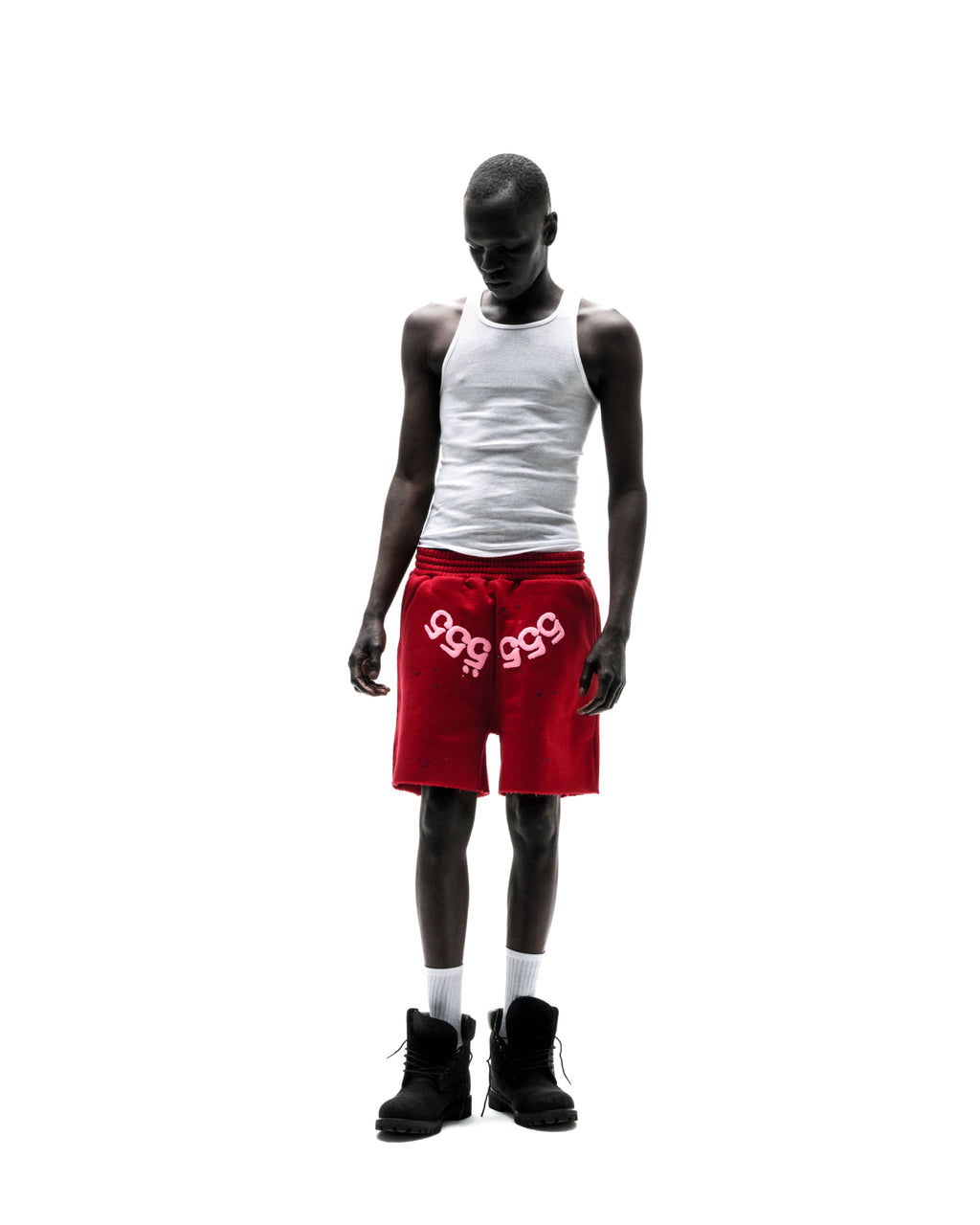 Model wears red 13oz cotton fleece Angel Number Shorts with "999" print, raw hem, and drawcord.