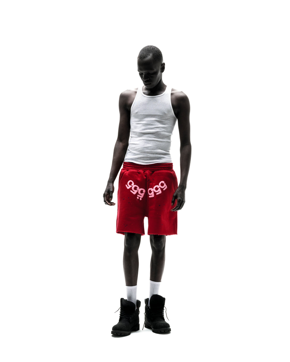 Model wears red 13oz cotton fleece Angel Number Shorts with "999" print, raw hem, and drawcord.