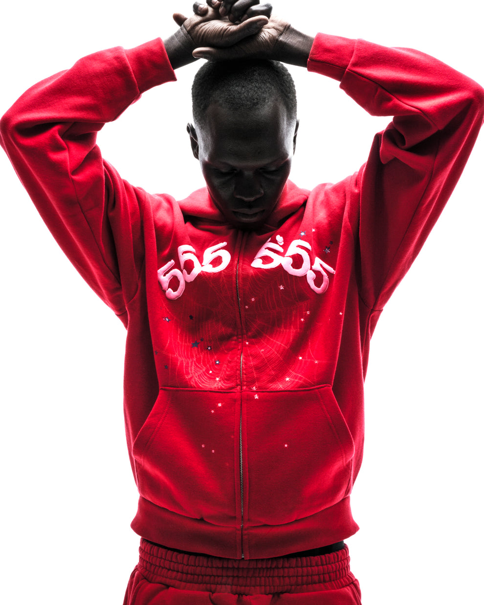 Model in red ANGEL NUMBER ZIP HOODIE with "555" puff print, scattered stars, and zip closure.