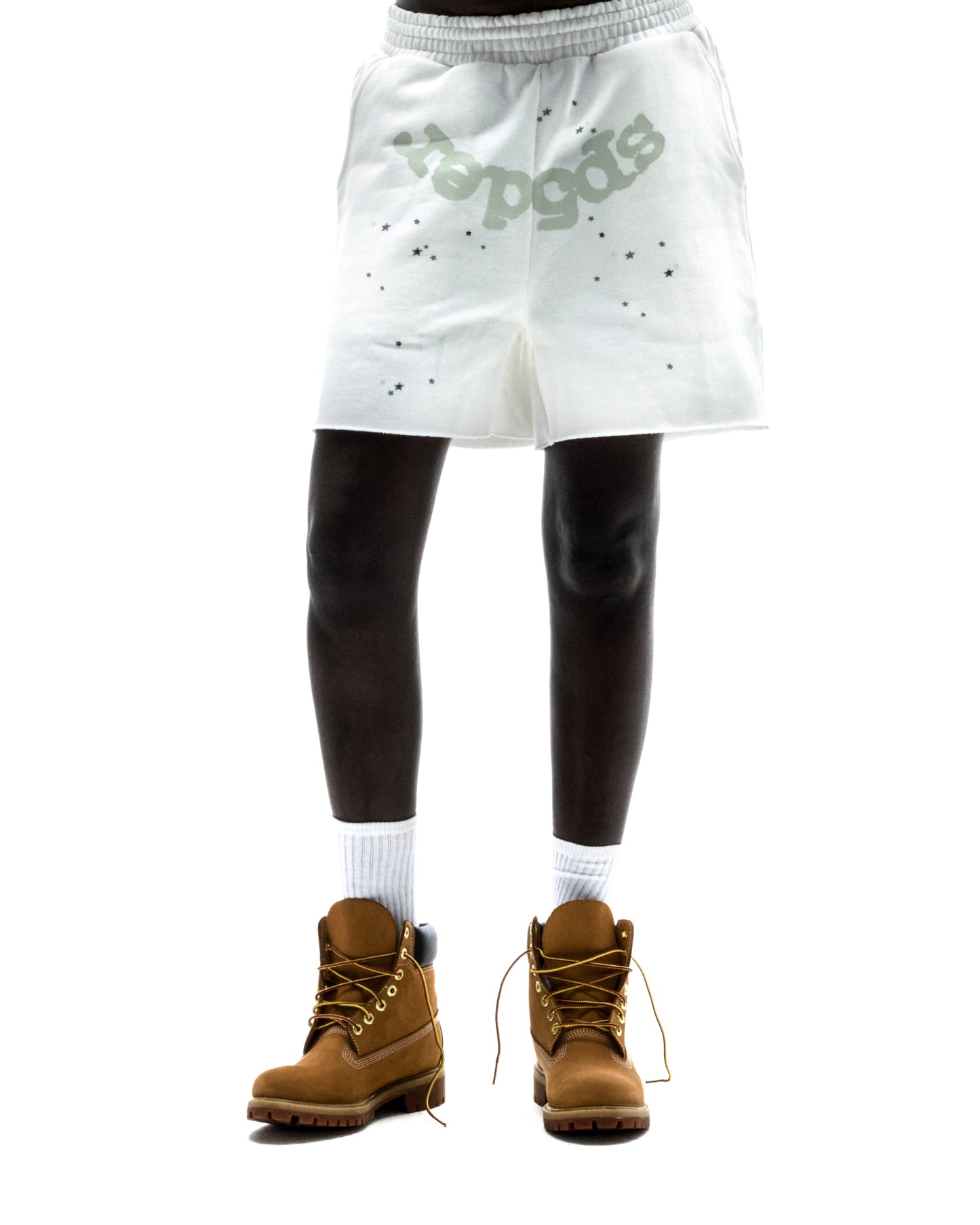 Model wearing white T&F SWEATSHORT with "SP5DER" text, scattered stars, raw hem, and brown boots.