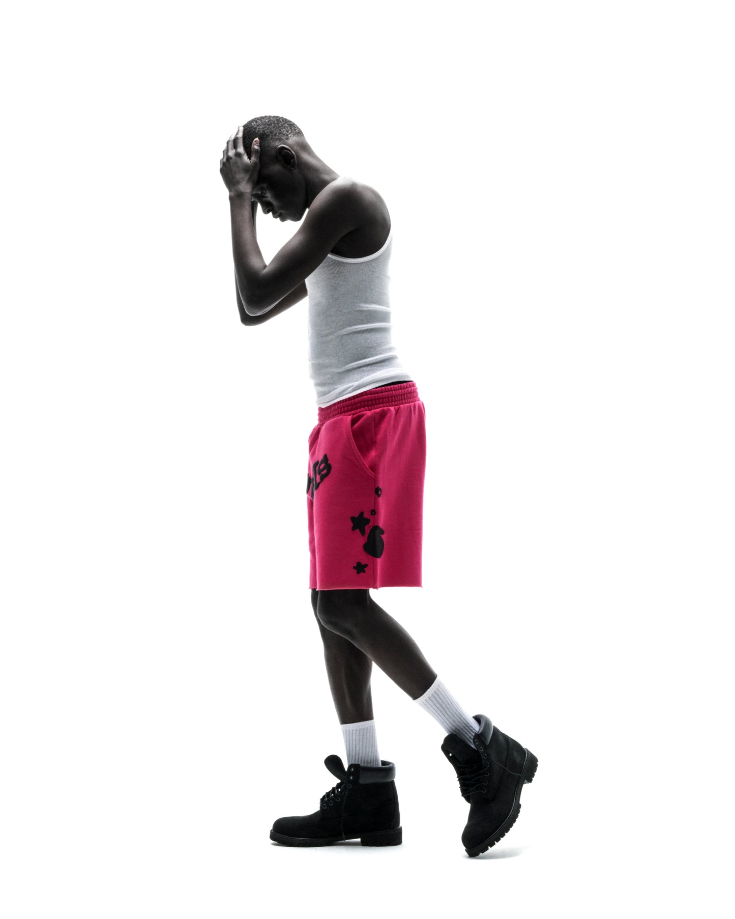 Model in pink Beluga print cotton fleece sweatshorts with raw hem, white tank top, and black boots.