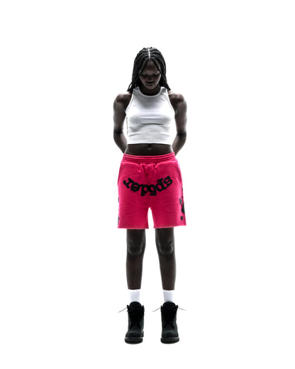 Model in hot pink Beluga sweatshorts with black print, white tank top, and black boots.