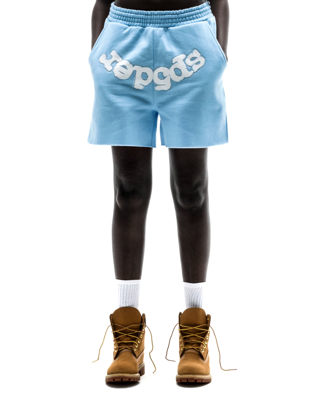 Model wearing light blue OG WEB SWEATSHORT with "SP5DER" text, raw hem, and brown boots.